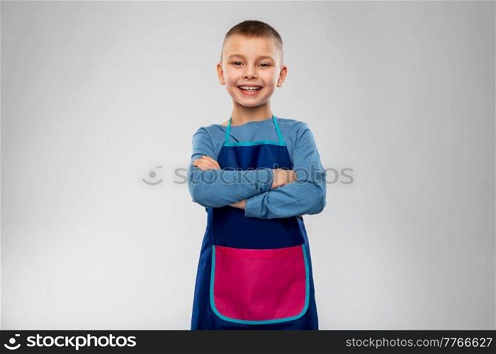 cooking, culinary and profession concept - happy smiling little boy in apron with crossed arms over grey background. smiling little boy in apron with crossed arms