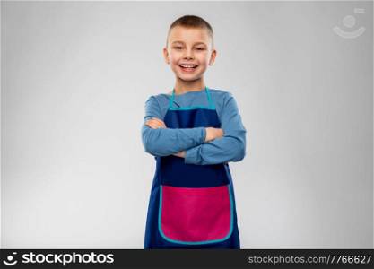 cooking, culinary and profession concept - happy smiling little boy in apron with crossed arms over grey background. smiling little boy in apron with crossed arms
