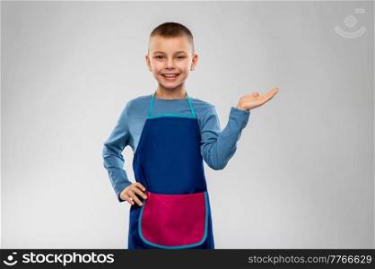 cooking, culinary and profession concept - happy smiling little boy in apron holding something imaginary on hand over grey background. little boy in apron holding something on hand