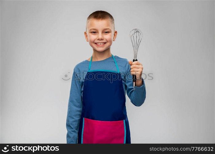 cooking, culinary and profession concept - happy smiling little boy in apron holding whisk over grey background. smiling little boy in apron holding whisk