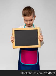 cooking, culinary and profession concept - happy smiling little boy in apron holding chalkboard over grey background. smiling little boy in apron holding chalkboard