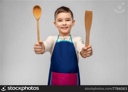 cooking, culinary and profession concept - happy smiling little boy in apron with wooden spoon and spatula over grey background. happy little boy in apron with spoon and spatula