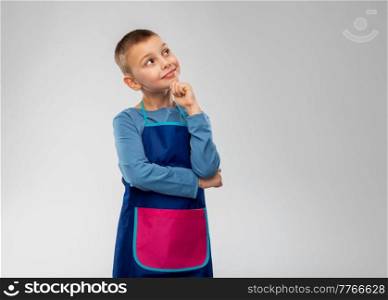 cooking, culinary and profession concept - happy smiling little boy in apron thinking over grey background. smiling little boy in apron thinking