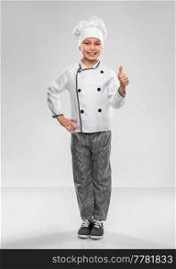 cooking, culinary and profession concept - happy smiling little boy in chef’s toque and jacket showing thumbs up over grey background. little boy in chef’s toque showing thumbs up