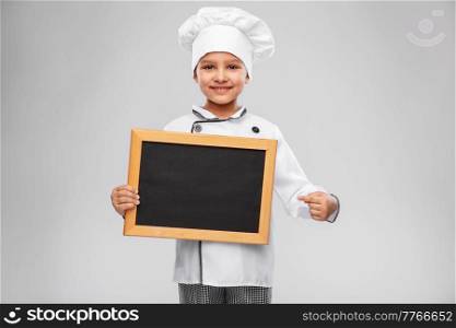cooking, culinary and profession concept - happy smiling little girl in chef&rsquo;s toque and jacket holding chalkboard over grey background. happy little girl in chef&rsquo;s toque with chalkboard