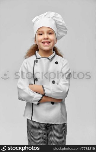 cooking, culinary and profession concept - happy smiling little girl in chef&rsquo;s toque and jacket over grey background. smiling little girl in chef&rsquo;s toque and jacket