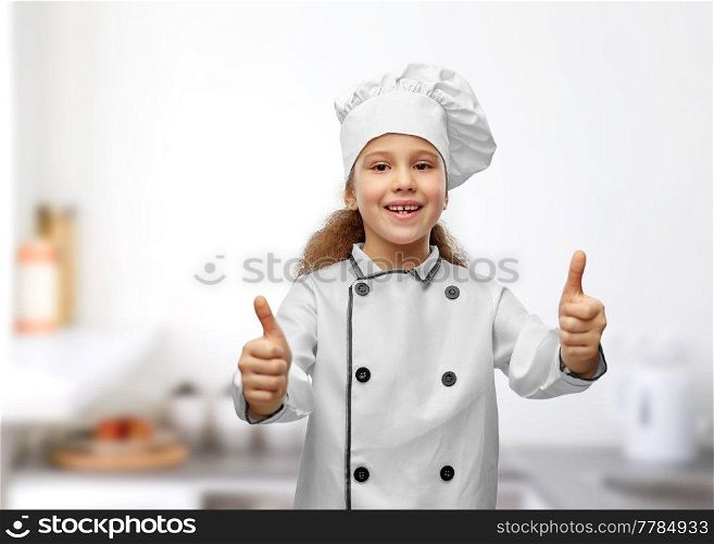 cooking, culinary and profession concept - happy smiling little girl in chef&rsquo;s toque and jacket showing thumbs up over restaurant kitchen background. little girl in chef&rsquo;s toque showing thumbs up