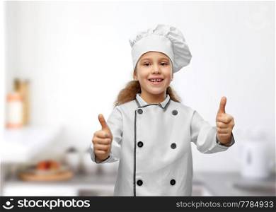 cooking, culinary and profession concept - happy smiling little girl in chef&rsquo;s toque and jacket showing thumbs up over restaurant kitchen background. little girl in chef&rsquo;s toque showing thumbs up