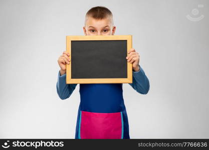 cooking, culinary and profession concept - little boy in apron holding chalkboard over grey background. little boy in apron holding chalkboard