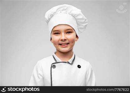 cooking, culinary and profession concept - portrait of happy smiling little boy in chef’s toque and jacket over grey background. smiling little boy in chef’s toque and jacket