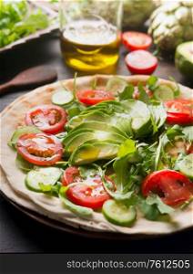 Cooking Delicious tortilla with cherry tomatoes, avocado, cucumber, arugula and olive oil. On a rustic wooden table, with ingredients laid out around. The idea of ??a healthy dish. Close up.