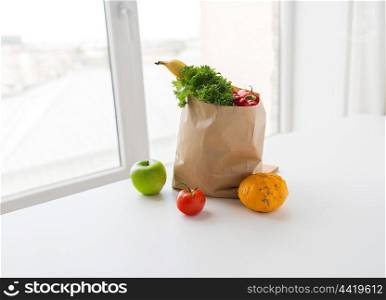 cooking, diet, vegetarian food and healthy eating concept - close up of paper bag with fresh ripe juicy vegetables, greens and fruits on kitchen table at home