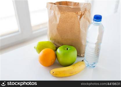 cooking, diet, vegetarian food and healthy eating concept - close up of paper bag with fresh ripe juicy fruits and water bottle on kitchen table at home
