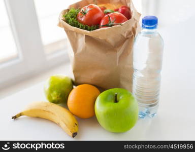 cooking, diet, vegetarian food and healthy eating concept - close up of paper bag with fresh ripe juicy fruits and vegetables and water bottle on kitchen table at home