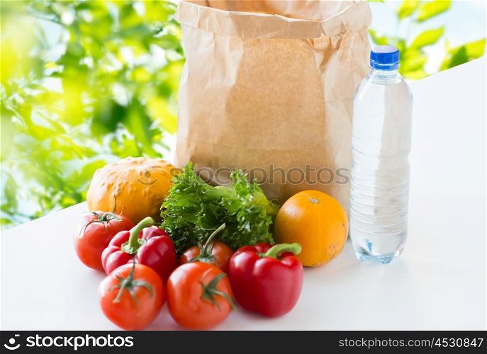cooking, diet, vegetarian food and healthy eating concept - close up of paper bag with fresh ripe juicy vegetables and water bottle on table over green natural background