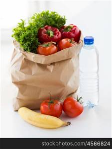 cooking, diet, vegetarian food and healthy eating concept - close up of paper bag with fresh ripe juicy fruits and vegetables and water bottle on kitchen table at home