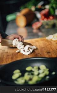 Cooking dinner. Chef holding a knife and cutting mushrooms on a wooden cutting board, close-up. Cooking dinner -  Chef Holding a Knife, Cutting Mushrooms on a Wooden Cutting Board