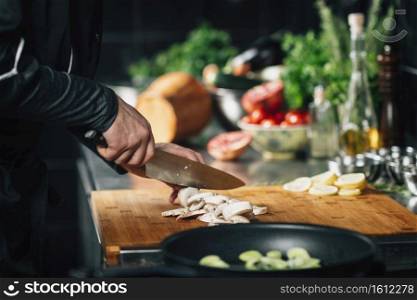 Cooking dinner. Chef holding a knife and cutting mushrooms on a wooden cutting board, close-up. Cooking dinner -  Chef Holding a Knife, Cutting Mushrooms on a Wooden Cutting Board