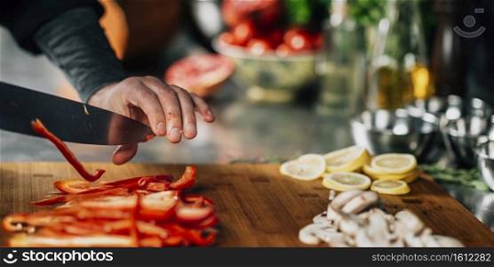 Cooking dinner. Chef holding a knife and cutting red bell pepper, close-up. Cooking dinner - Chef Holding a Knife and Cutting Red Bell Pepper
