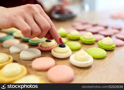 cooking, food and baking concept - chef decorating macarons shells at confectionery or pastry shop. chef decorating macarons shells at pastry shop