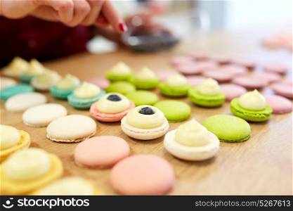 cooking, food and baking concept - chef decorating macarons shells at confectionery or pastry shop. chef decorating macarons shells at pastry shop