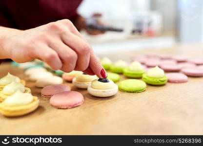 cooking, food and baking concept - chef decorating macarons shells at confectionery or pastry shop. chef decorating macarons shells at pastry shop