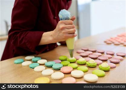 cooking, food and baking concept - chef with confectionery bag squeezing cream filling to macarons shells at pastry shop. chef with injector squeezing filling to macarons
