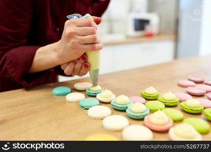 cooking, food and baking concept - chef with confectionery bag squeezing cream filling to macarons shells at pastry shop kitchen. chef with injector squeezing filling to macarons