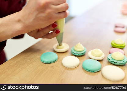 cooking, food and baking concept - chef with confectionery bag squeezing cream filling to macarons shells at pastry shop. chef with injector squeezing filling to macarons