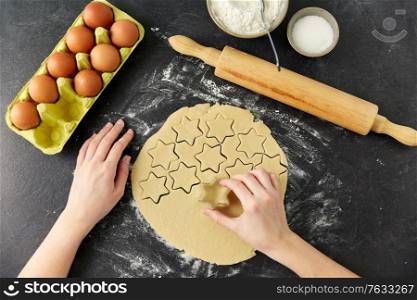 cooking food and culinary concept - hands cutting shortcrust pastry dough with star shaped cutter on table. hands cutting dough with star mold on table