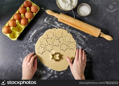 cooking food and culinary concept - hands, shortcrust pastry dough cut with star shaped cutter, rolling pin, eggs and flour on table. hands with shortcrust pastry dough and star mold