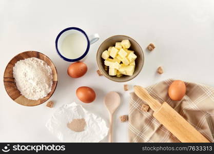 cooking food and culinary concept - rolling pin, butter, eggs, flour and cane sugar on table. rolling pin, butter, eggs, flour, milk and sugar