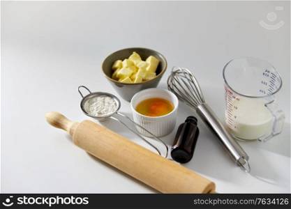 cooking food and culinary concept - rolling pin, butter, eggs, flour and whisk on table. rolling pin, butter, eggs, flour, milk and whisk