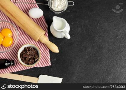 cooking food and culinary concept - rolling pin, milk, eggs, flour and chocolate on table. rolling pin, milk, eggs, flour and chocolate