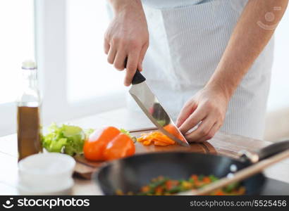 cooking, food and home concept - close up of male hand cutting pepper on cutting board at home