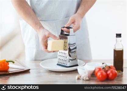 cooking, food and home concept - close up of male hands grating cheese
