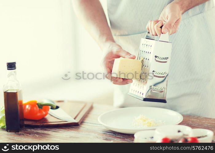 cooking, food and home concept - close up of male hands grating cheese