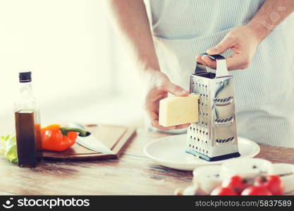 cooking, food and home concept - close up of male hands grating cheese