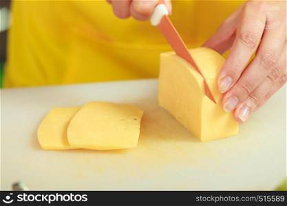 Cooking, food and home concept. Woman hands cutting piece of cheese on kitchen board close up
