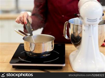 cooking, food and kitchen appliances concept - chef with stand mixer and thermometer measuring temperature in sugar syrup boiling in pot on stove at kitchen. chef measuring temperature in pot at kitchen