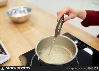 cooking, food and kitchen appliances concept - chef with thermometer measuring temperature in sugar syrup boiling in pot on stove . chef measuring temperature in syrup at kitchen