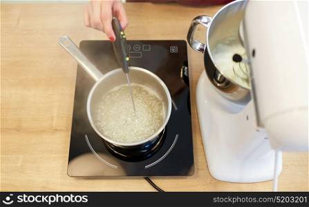 cooking, food and kitchen appliances concept - electric mixer and pot on stove. chef measuring temperature in syrup at kitchen