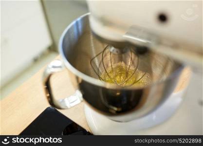 cooking, food and kitchen appliances concept - electric mixer whipping egg whites. electric mixer whipping egg whites at kitchen