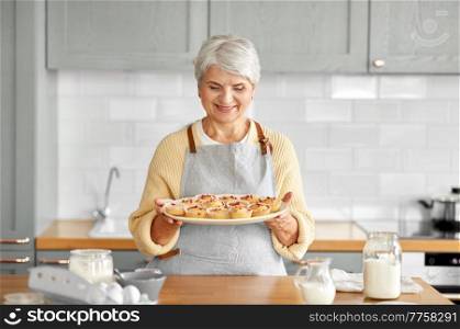 cooking food, baking and culinary concept - happy smiling senior woman holding big plate with cupcakes on kitchen at home. woman holding plate with cupcakes on kitchen