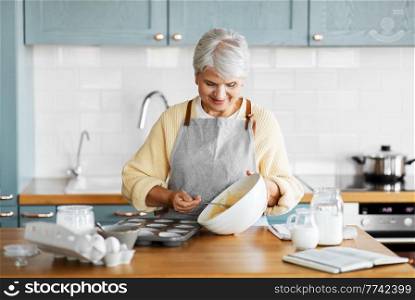 cooking food, baking and culinary concept - happy smiling woman distributing batter into cake molds on kitchen at home. woman putting batter into baking molds on kitchen
