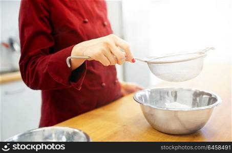 cooking food, baking and people concept - chef with strainer sieving flour into bowl and making batter or dough. chef with flour in bowl making batter or dough