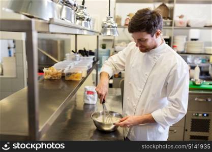 cooking food, baking and people concept - happy male chef cook whipping dough or batter by whisk in bowl at restaurant or bakery kitchen. happy male chef cooking food at restaurant kitchen