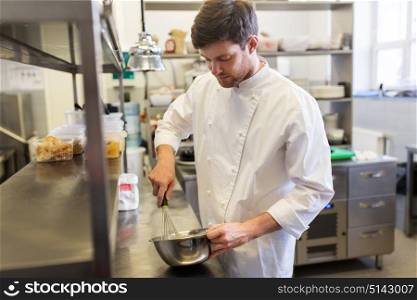 cooking food, baking and people concept - happy male chef cook whipping dough or batter by whisk in bowl at restaurant or bakery kitchen. happy male chef cooking food at restaurant kitchen