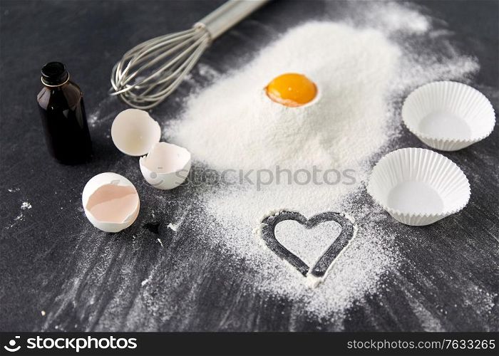 cooking food, culinary and recipe concept - egg on heap of flour, whisk and paper baking molds on table. flour, egg, whisk and paper baking molds on table
