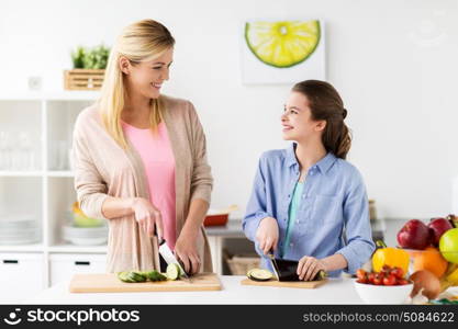 cooking food, healthy eating, family and people concept - happy mother and daughter chopping vegetables for dinner at home kitchen. happy family cooking dinner at home kitchen. happy family cooking dinner at home kitchen